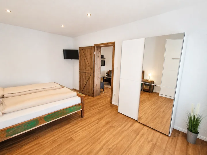 Schlafzimmer in Wohnung 6 mit Bett, Holzschiebetür und verspiegeltem Kleiderschrank